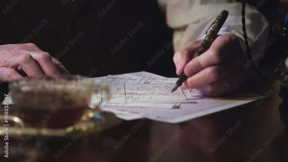 Close up scene tracking right across hands of a 1930s businessman with fountain pen making entries into a ledger.