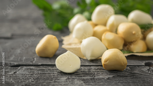 Freshly prepared smoked and regular mozzarella cheese in paper on a dark wooden table.