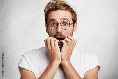 Terrified nervous male job applicant feels anxious before interview with employee, bites nails as worries much, isolated over white studio background. Emotional troublesome frustrated student