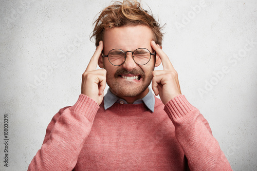 Desperate handsome young clever student tries to remember learned information for exam, bites lips, closes eyes and keeps finger on temples, concentrates on topic, isolaed over white background