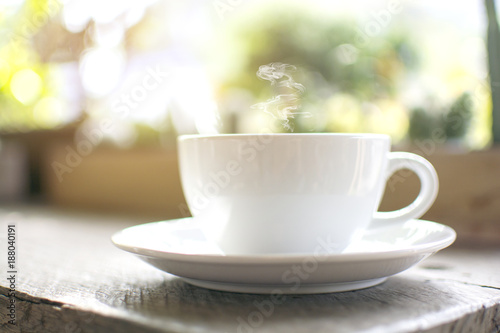 Close up a steaming white cup of hot cappuccino with bokeh tree background