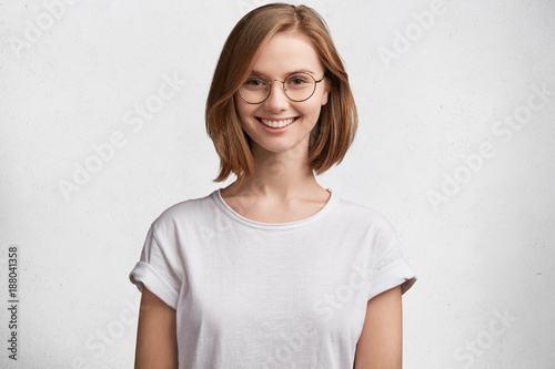 Attractive young lady or female diligent student with short hair, has shining smile, being pleased to recieve high grant for hard work and participation in various contest, dressed casually. © wayhome.studio 