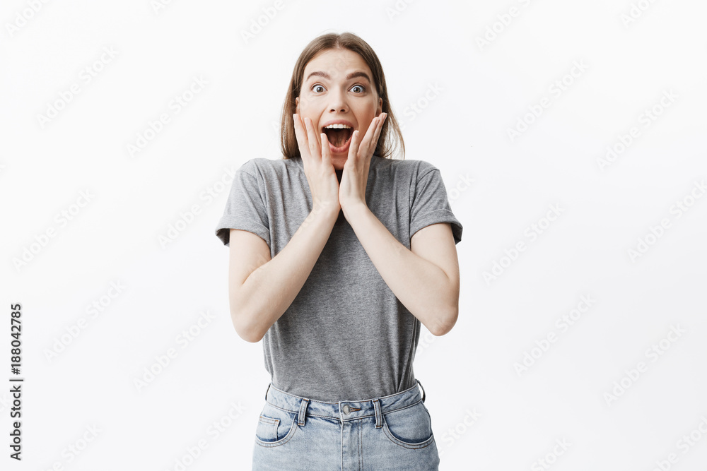Portrait of young good looking student girl with dark hair in fashionable clothes squeezing face with hands in excitement with opened mouth seeing pop star on street. Portrait of young good looking student girl with dark hair in fashionable clothes squeezing face with hands in excitement with opened mouth seeing pop star on street.