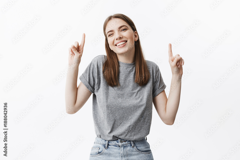 Copy space. Portrait of joyful beautiful dark-haired female student smiling with teeth, looking in camera with satisfied and excited expression, pointing upside with fingers on both hands. Copy space. Portrait of joyful beautiful dark-haired female student smiling with teeth, looking in camera with satisfied and excited expression, pointing upside with fingers on both hands.
