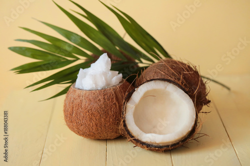 Natural coconut oil. Coconut in a cut and coconut oil pieces in the coconut shell and palm leaves on a yellow wooden board background 