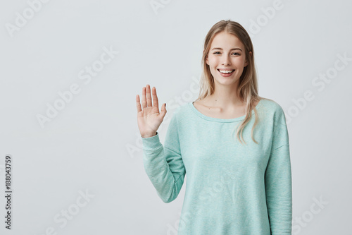 Young beautiful woman with long blonde hair congratulating her friend on her birthday. Pretty student girl saying hello  smiling joyfully and friendly  waving her hand