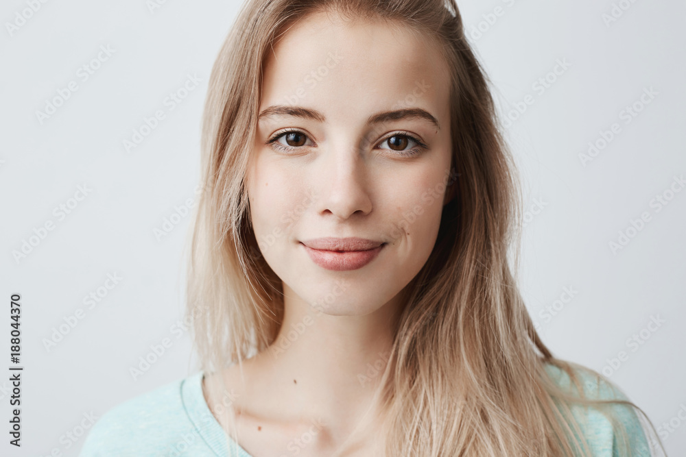 Fototapeta premium Beautiful female having dark shining eyes, pure skin and blonde straight hair wearing loose sweater looking directly at camera having mysterious and glad expression. Face expressions and emotions