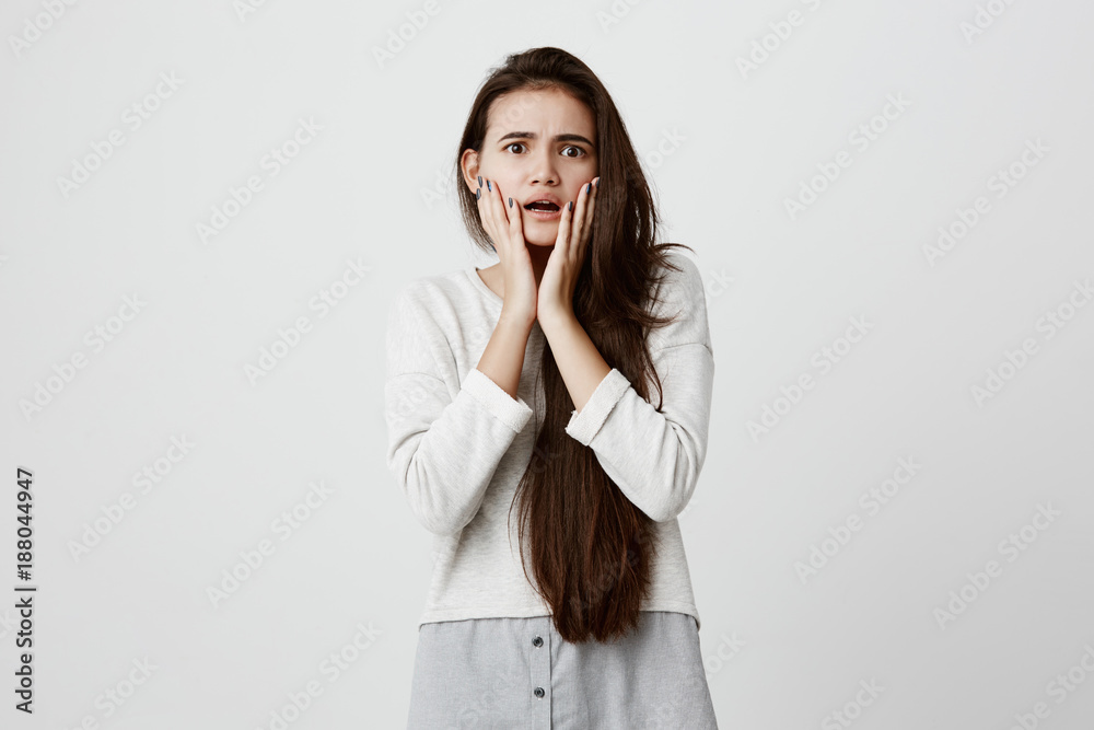 Emotional worried brunette girl holding hands on her cheeks, opening mouth, feeling perplexed and frustrated after she left home without having unplugged iron. Human emotions and feelings Emotional worried brunette girl holding hands on her cheeks, opening mouth, feeling perplexed and frustrated after she left home without having unplugged iron. Human emotions and feelings