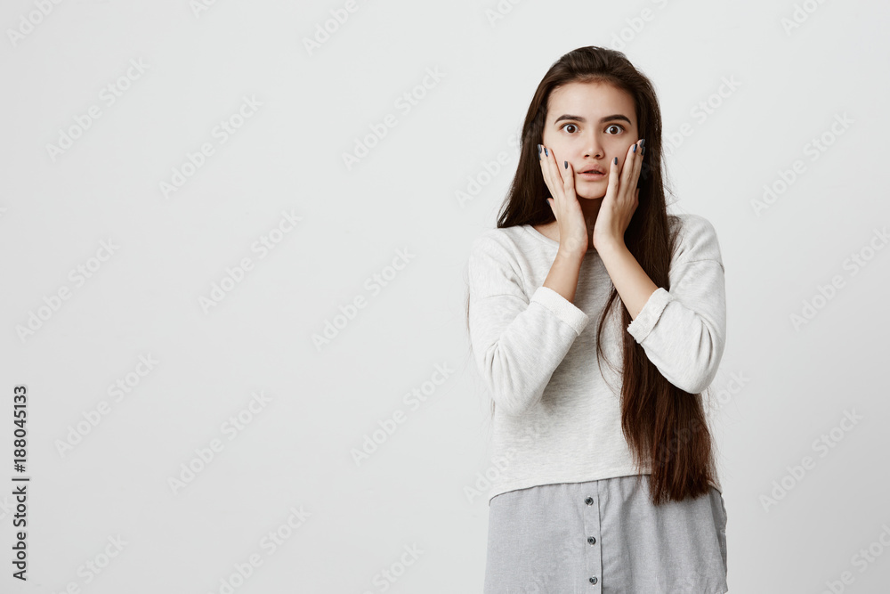 Shocked stunned emotional brunette girl keeps hands on cheeks, being troubled to listen advices of his parents. European young female with long dark hair can`t believe in shocking news Shocked stunned emotional brunette girl keeps hands on cheeks, being troubled to listen advices of his parents. European young female with long dark hair can`t believe in shocking news