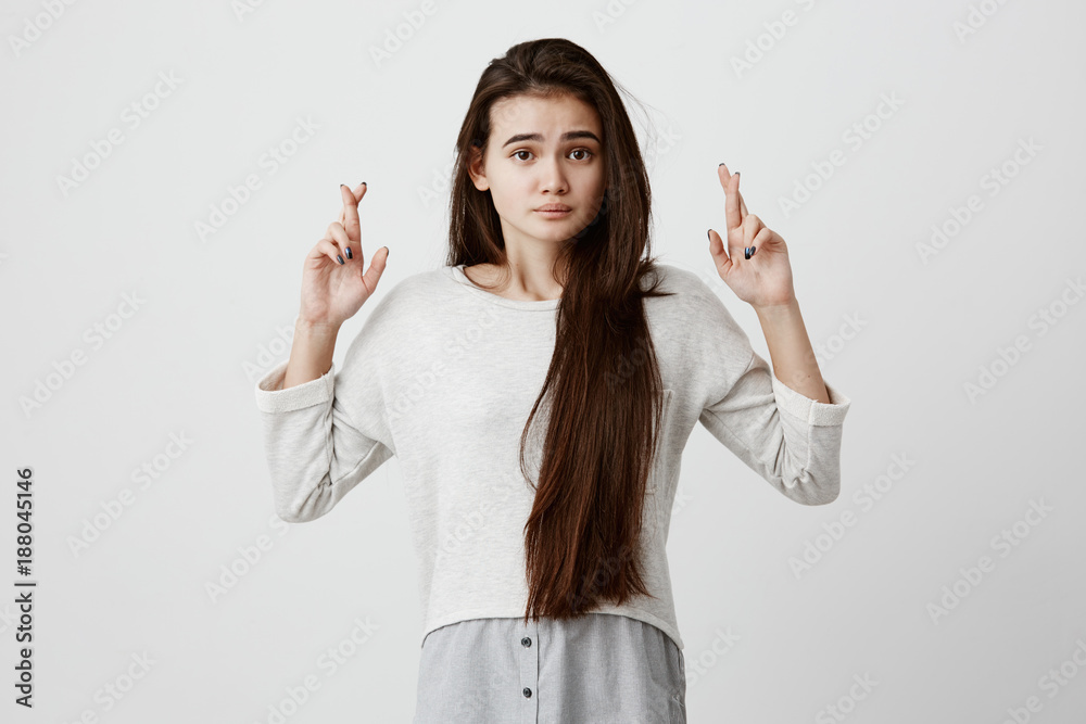 Indoor shot of beautiful brunette girl with long hair having excited, superstitious and naive look, keeping fingers crossed, hoping for good luck before passing exam. Body language and gestures Indoor shot of beautiful brunette girl with long hair having excited, superstitious and naive look, keeping fingers crossed, hoping for good luck before passing exam. Body language and gestures