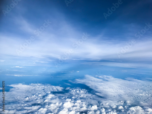 Aerial view among the sea of white clouds and deep blue sea with the blue sky from the seat of passenger in Airplane during the journey