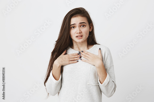 Excited astonished cute girl with long dark straight hair putting hands on breast, in casual clothes, didn`t expect to receive present from parents. Emotions, feelings, face expression concept photo