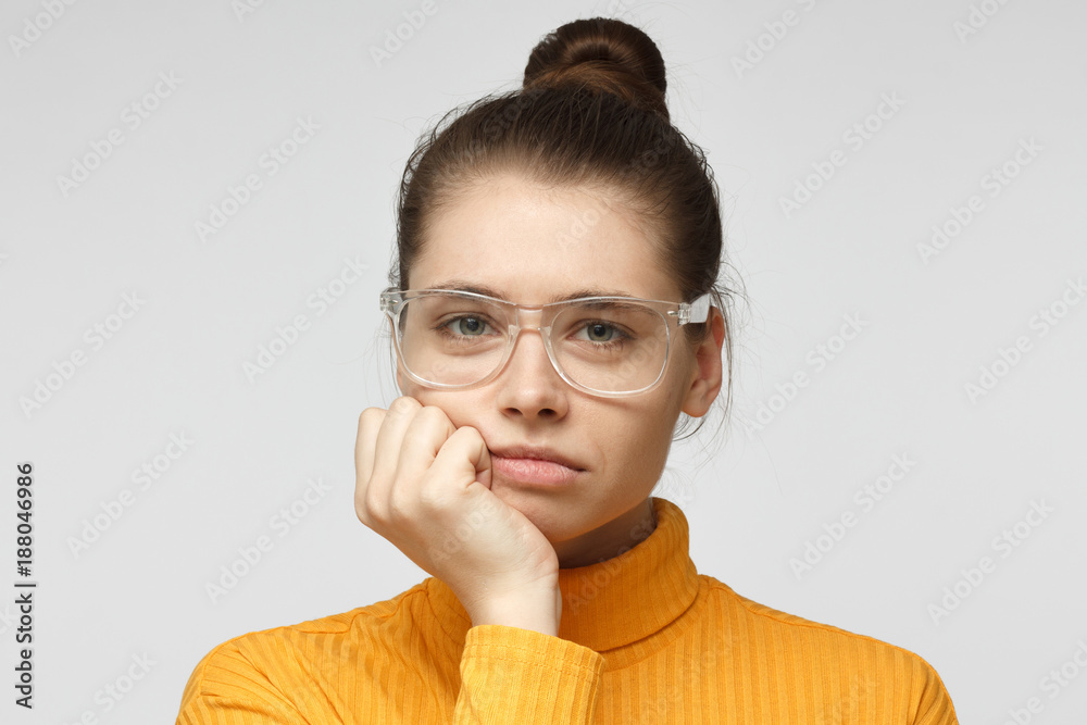 Close up portrait of bored young female in glasses with head on chin isolated on gray background Close up portrait of bored young female in glasses with head on chin isolated on gray background