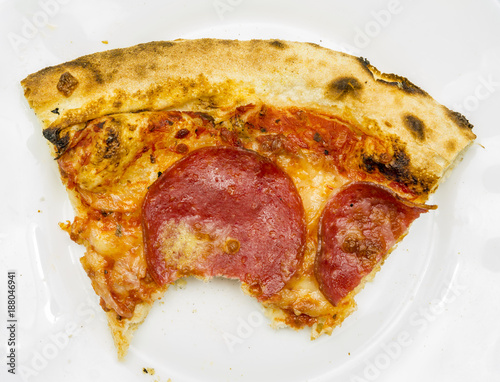 Closeup of a bitten portion of pizza on a white plate.