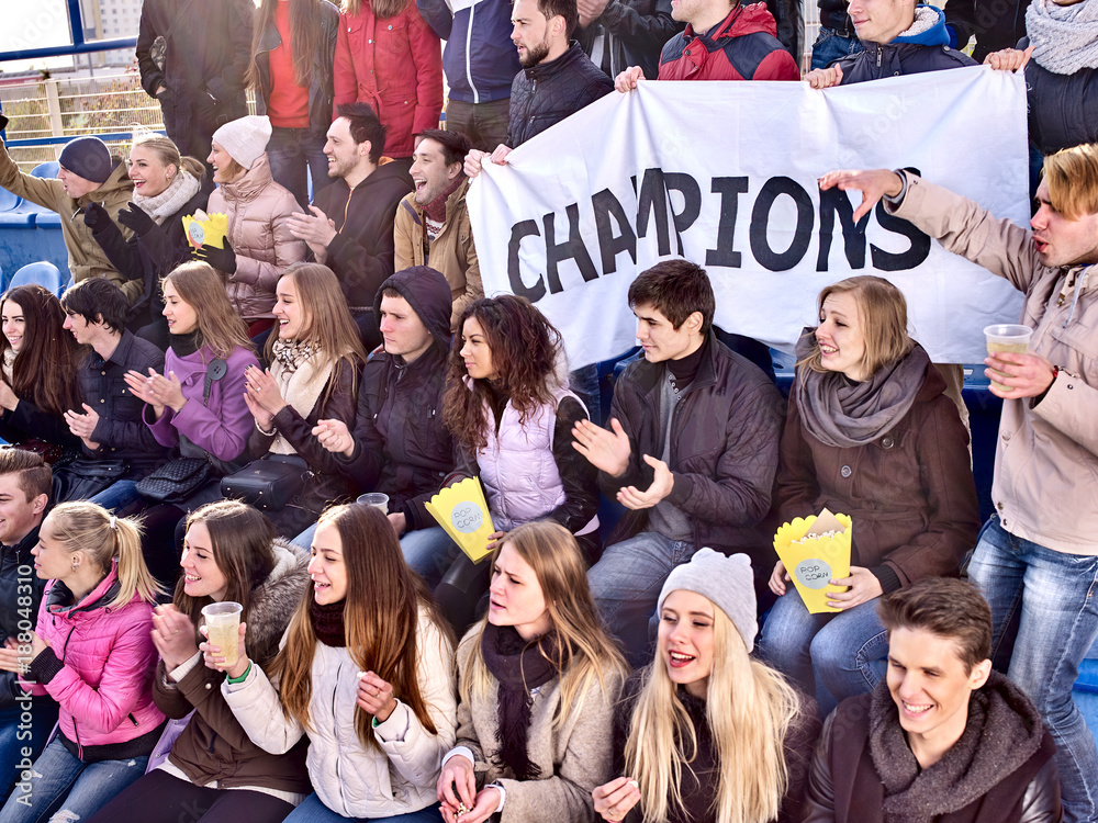 Fans cheering in stadium holding champion banner and singing on tribunes. Soccer game. People holding banner with Champion banner happily eating popcorn.