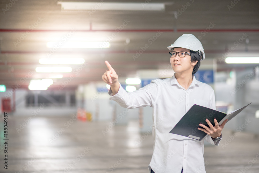 Young Asian Engineer or Architect holding files and pointing his hand while wearing personal protective equipment safety helmet at construction site. Engineering and building construction concepts Young Asian Engineer or Architect holding files and pointing his hand while wearing personal protective equipment safety helmet at construction site. Engineering and building construction concepts