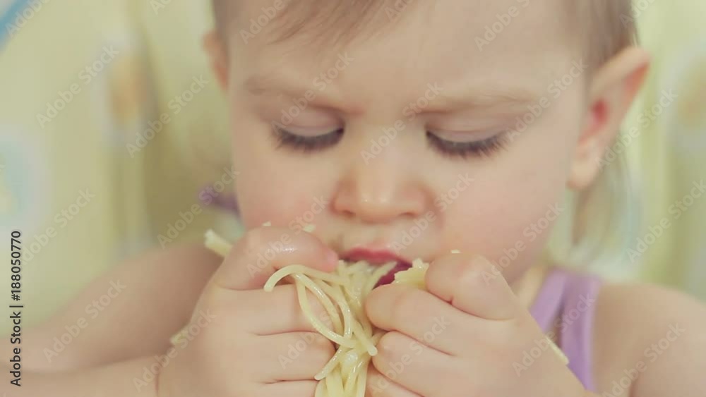 Charming little girl eating spaghetti with her fingers and enjoying it Charming little girl eating spaghetti with her fingers and enjoying it
