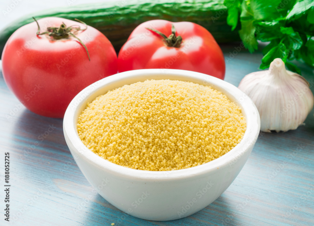Moroccan couscous in bowl, blue wooden background, rustic style, selective focus, side view. Heap of raw cous and vegetable. Moroccan couscous in bowl, blue wooden background, rustic style, selective focus, side view. Heap of raw cous and vegetable.