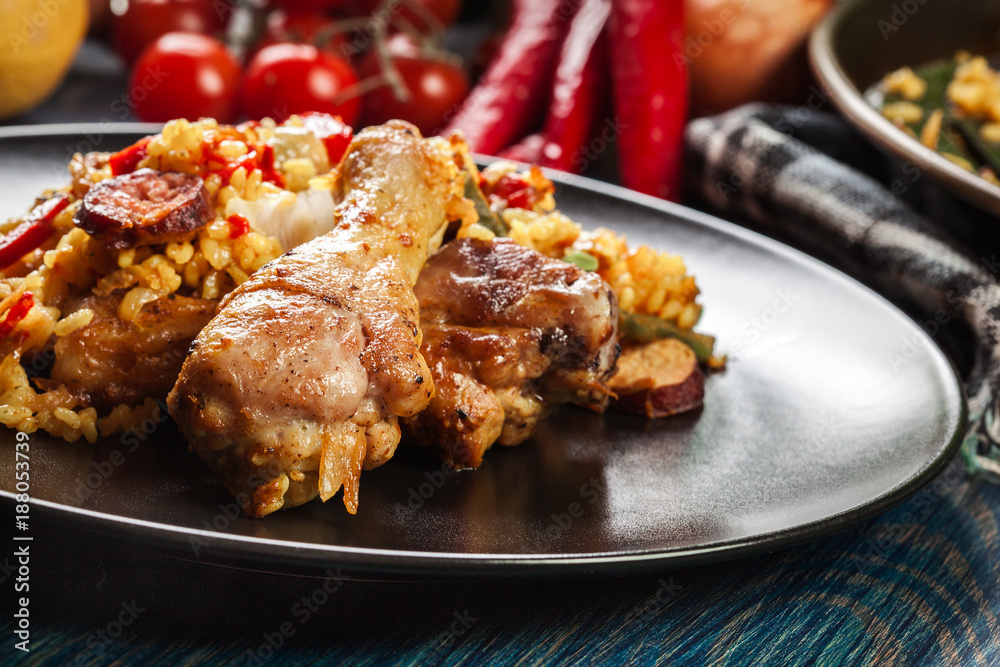 Traditional paella with chicken legs, sausage chorizo and vegetables served on black plate