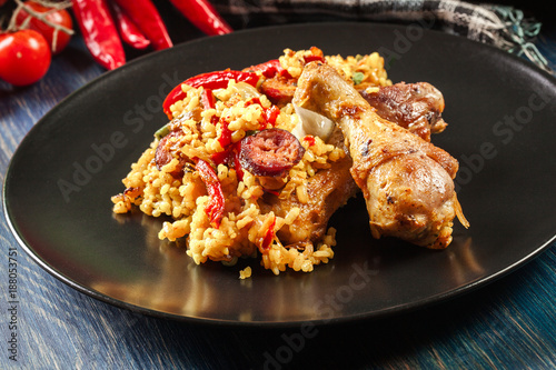 Traditional paella with chicken legs, sausage chorizo and vegetables served on black plate