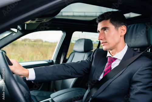 Man driving his car for business travel wearing a suit © Kzenon