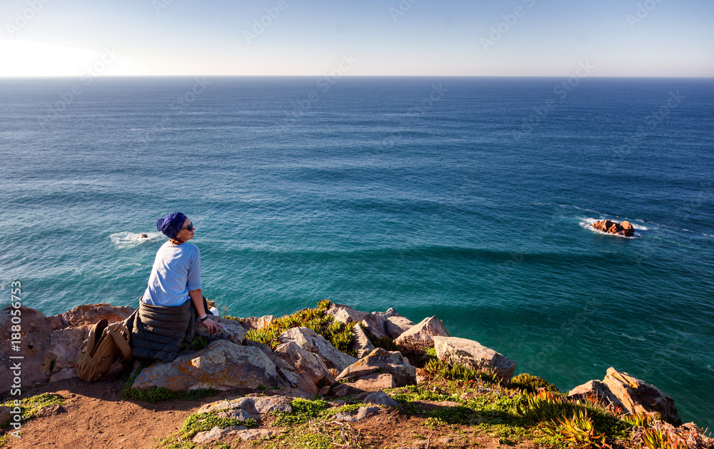 young beautiful woman sits on a stone on the background of Cape Cabo da Roca, Portugal, Coast of the Atlantic Ocean. Freedom, youth, travel young beautiful woman sits on a stone on the background of Cape Cabo da Roca, Portugal, Coast of the Atlantic Ocean. Freedom, youth, travel