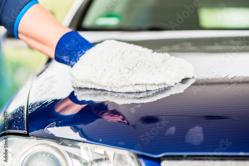 Close-up of male hand wiping the wet surface of a blue car with microfiber wash mitt for drying photo