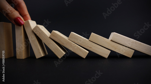 Management intervention or decision suggested by businesswoman hand stopping the negative continuous effects, with wooden blocks as dominoes on black background 