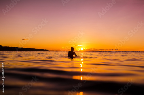 Sunset in Bali and surfer waiting for wave