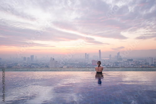 Photography Young lady watching the sunrise at the infinity pool with city view