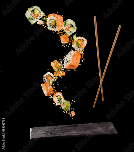 Flying pieces of sushi with wooden chopsticks and stone plate, isolated on black background.