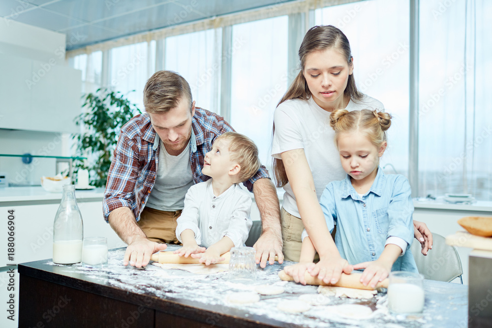 Father, mother, daughter and son rolling dough for homemade pastry on table Father, mother, daughter and son rolling dough for homemade pastry on table