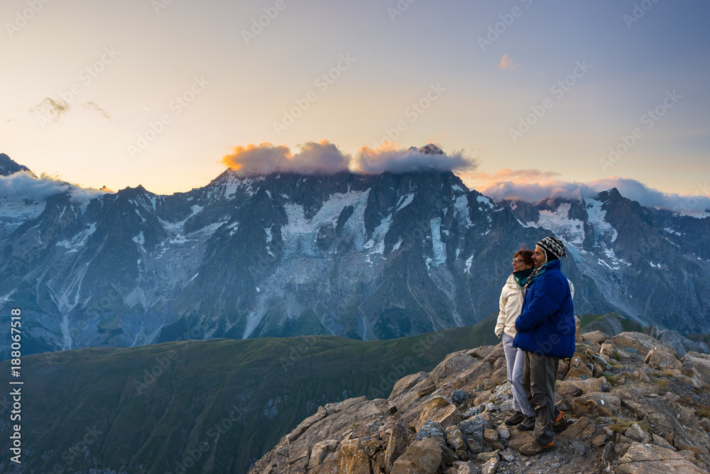 Couple of people looking at the sunrise over Mont Blanc mountain peak (4810 m). Valle d'Aosta, italian summer adventures and travel destination on the Alps.