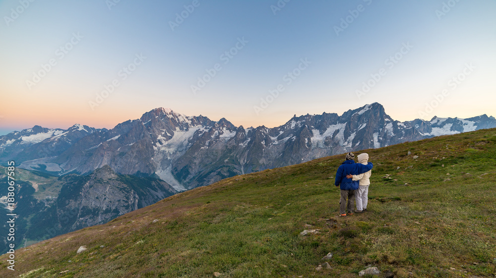 Couple of people looking at the sunrise over Mont Blanc mountain peak (4810 m). Valle d'Aosta, italian summer adventures and travel destination on the Alps.