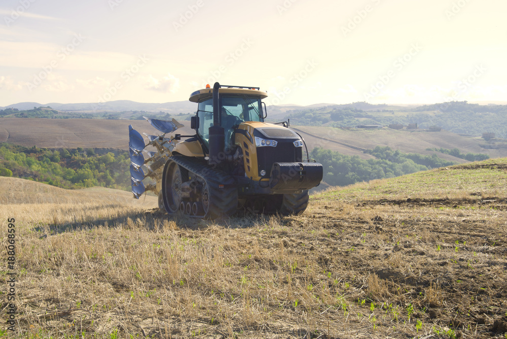 Yellow caterpillar tractor with a plow driving along the harvested field Yellow caterpillar tractor with a plow driving along the harvested field