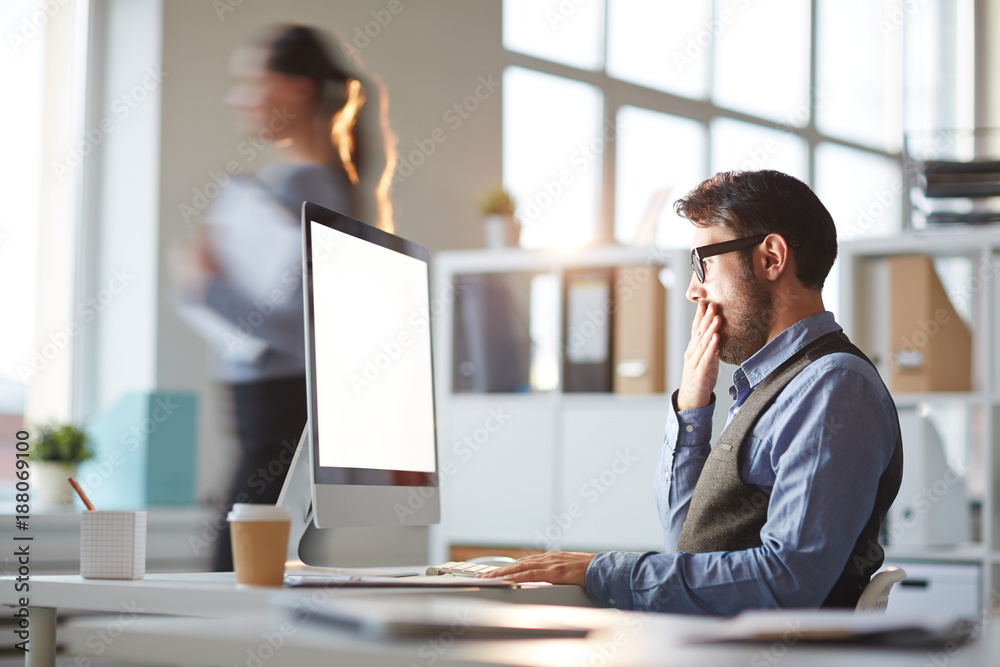 Businessman yawning by workplace while working in front of computer monitor Businessman yawning by workplace while working in front of computer monitor
