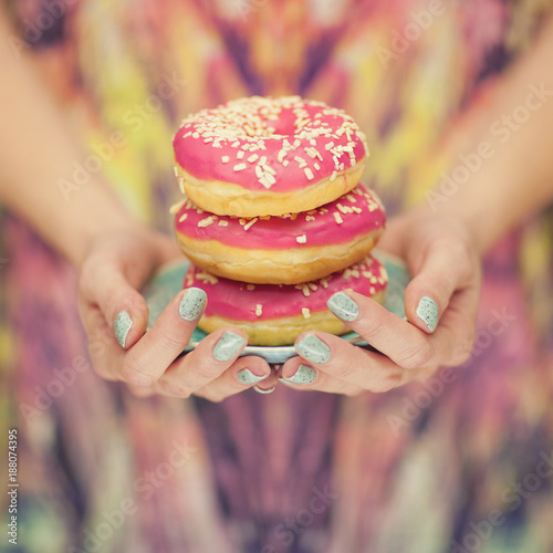 Woman hands with turquoise nail polish holding a plate with pink donuts with pink pattern background