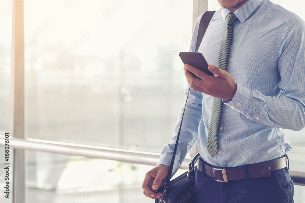 Fototapeta premium Portrait of a confident man. Entrepreneur working on phone while standing in modern office interior. Intelligent male lawyer holding phone. Businessman using cell phone in the airport terminal.