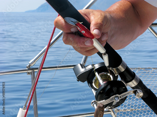 Sea fishing on yacht. Fisherman is holding spinning rod in tanned hand. Close-up spinning reel and fishing hook.