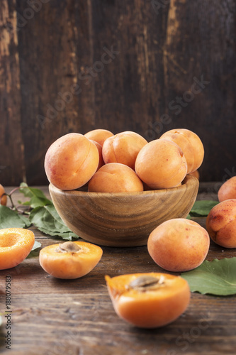 ripe apricots with leaves in a wooden plate on a wooden background