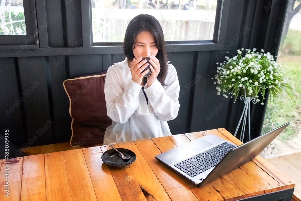 An Asian girl in white shirt plays notebook on wooden table in black room. An Asian girl in white shirt plays notebook on wooden table in black room.