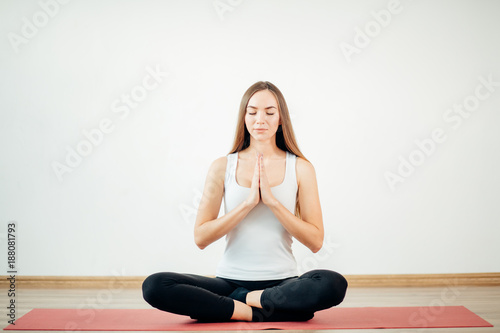 Young attractive woman practicing yoga, sitting in Padmasana, exercise, Lotus pose, namaste