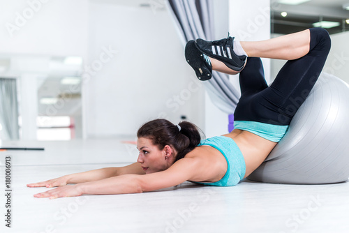 Young brunette stretching her back trying to reach head with feet from laying position with arms extended forward in sports club