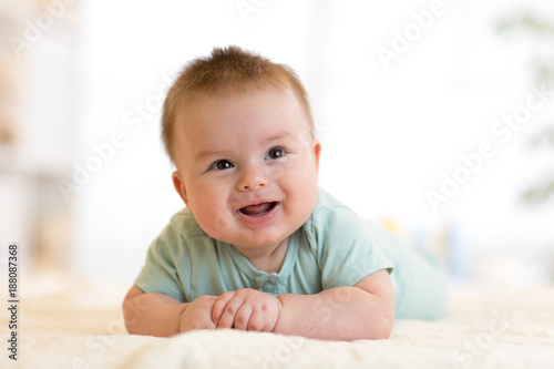 Very happy laughing baby in blue clothes lying on his belly.