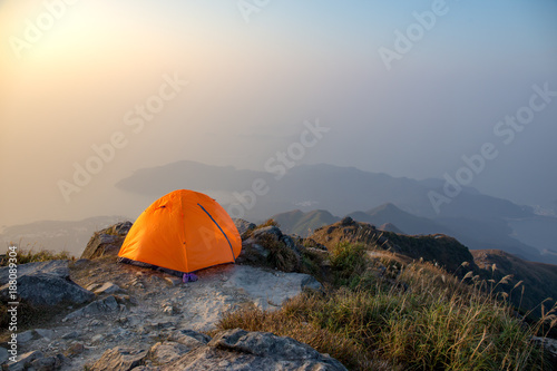 orange tent camping near cliff isolated on lantau peak, Hong Kong in sunrise and fog with copy space