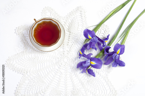 Fototapeta Naklejka Na Ścianę i Meble -  Violet Irises xiphium (Bulbous iris, sibirica) with cup of tea on white background with space for text. Top view, flat . Holiday greeting card for Valentine's Day, Woman's Day, Mother's Day, Easter!