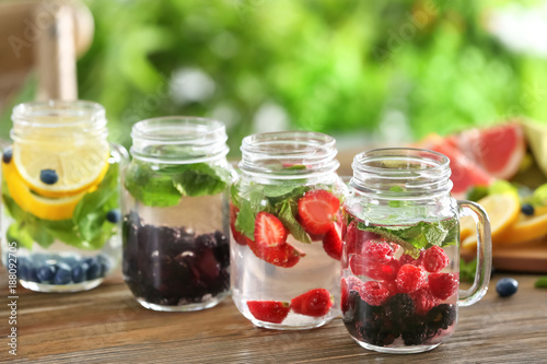 Mason jars of infused water with fruits and berries on wooden table