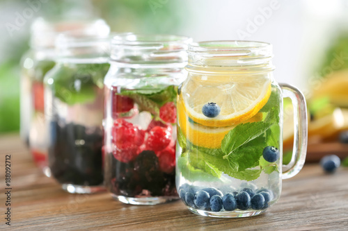 Mason jars of infused water with fruits and berries on wooden table