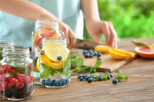 Blurred view of woman preparing infused water with fruits and berries in mason jar photo