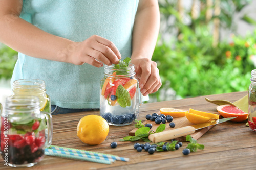 Woman preparing infused water with fruits and berries in mason jar